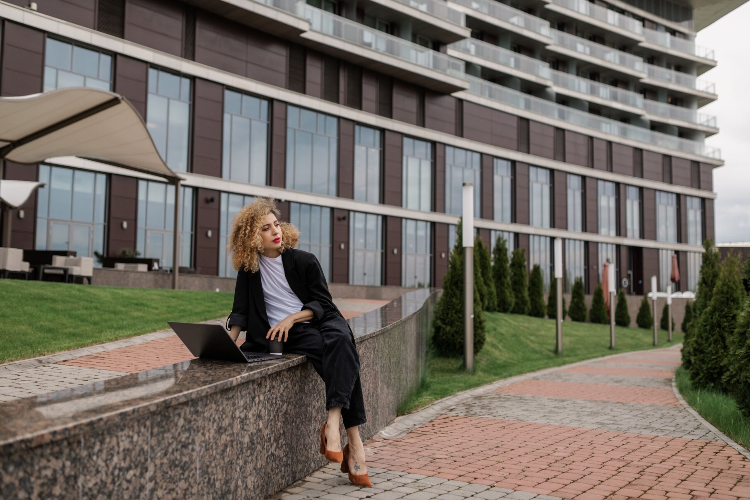 Businesswoman using a laptop outside a modern building, symbolizing independent professional work