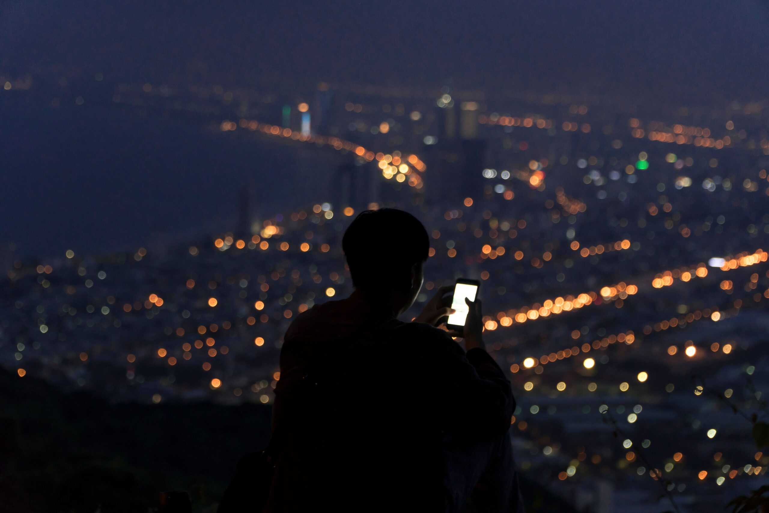 Silhouette of a person using a smartphone against a city night skyline